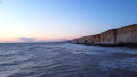 Sunset-drone-shot-tall-chalk-cliff-by-the-seaside-in-Brighton,-England