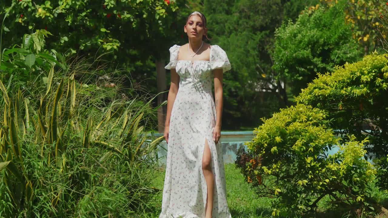 A girl in a breezy dress strolling in a lush tropical park on a sunny day.