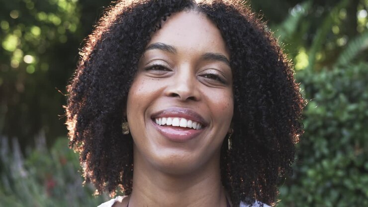 Mulher afro-americana reagindo à deixa da câmera, sorrindo, rindo no quintal, usando brincos de ouro.