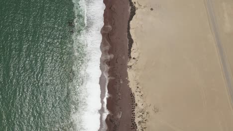 Vertical-aerial-pattern:-Green-ocean-waves-onto-desert-cliff-sand