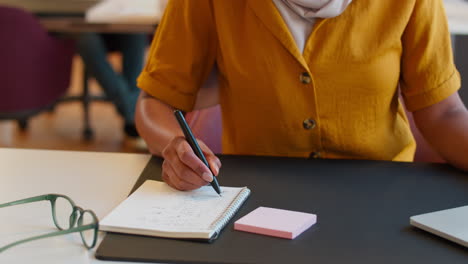 mujer de negocios madura con pañuelo en la cabeza trabajando en el escritorio en la oficina escribiendo en el cuaderno