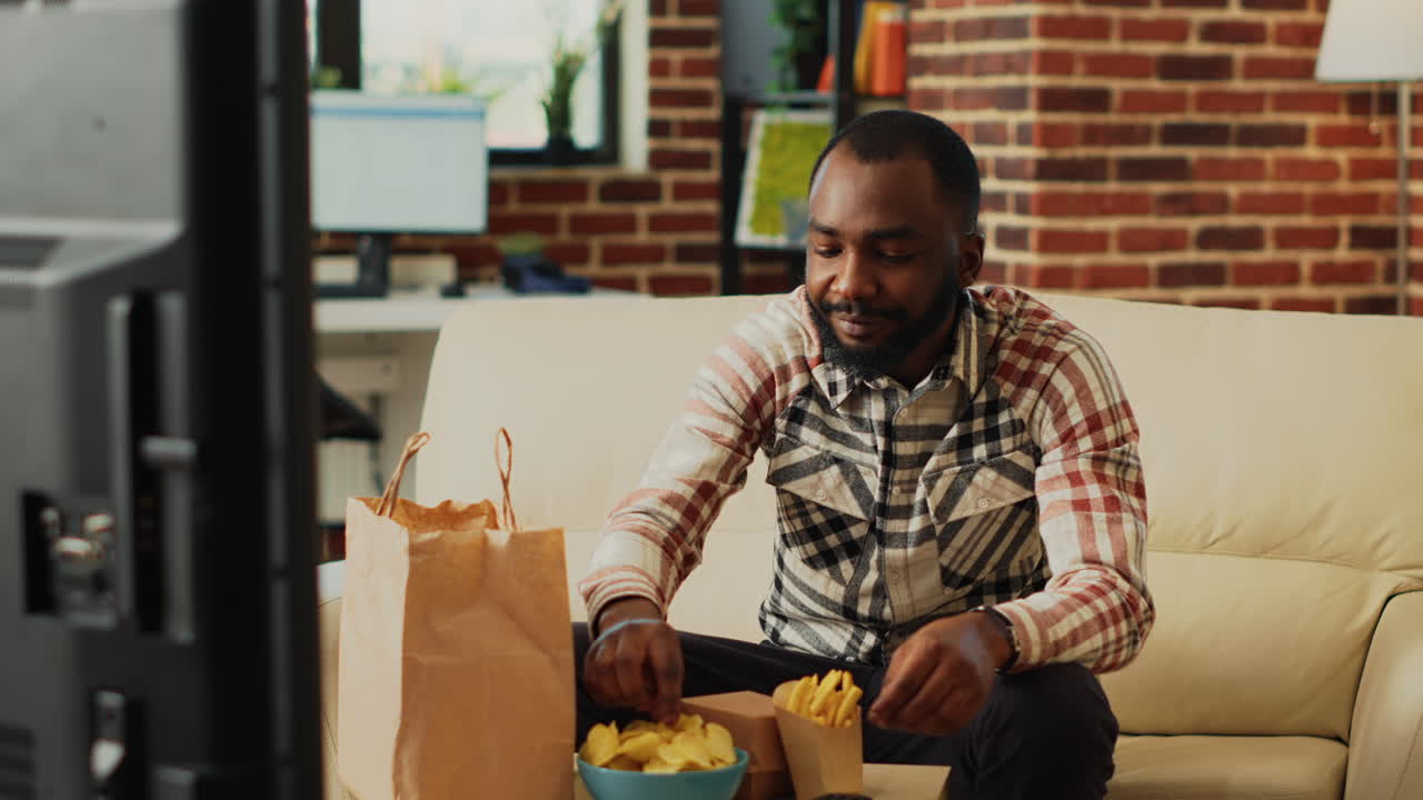 Cheerful person taking bite of cheeseburger on couch