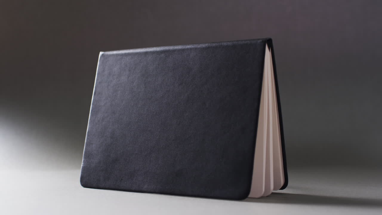 Close up of open black book standing horizontal with copy space on gray background in slow motion