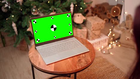 woman in christmas communicates on video call using laptop with green screen.