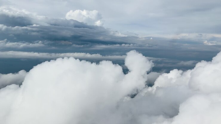 Smooth aerial flight above bright cumulus cloud tops under soft, overcast daylight sky