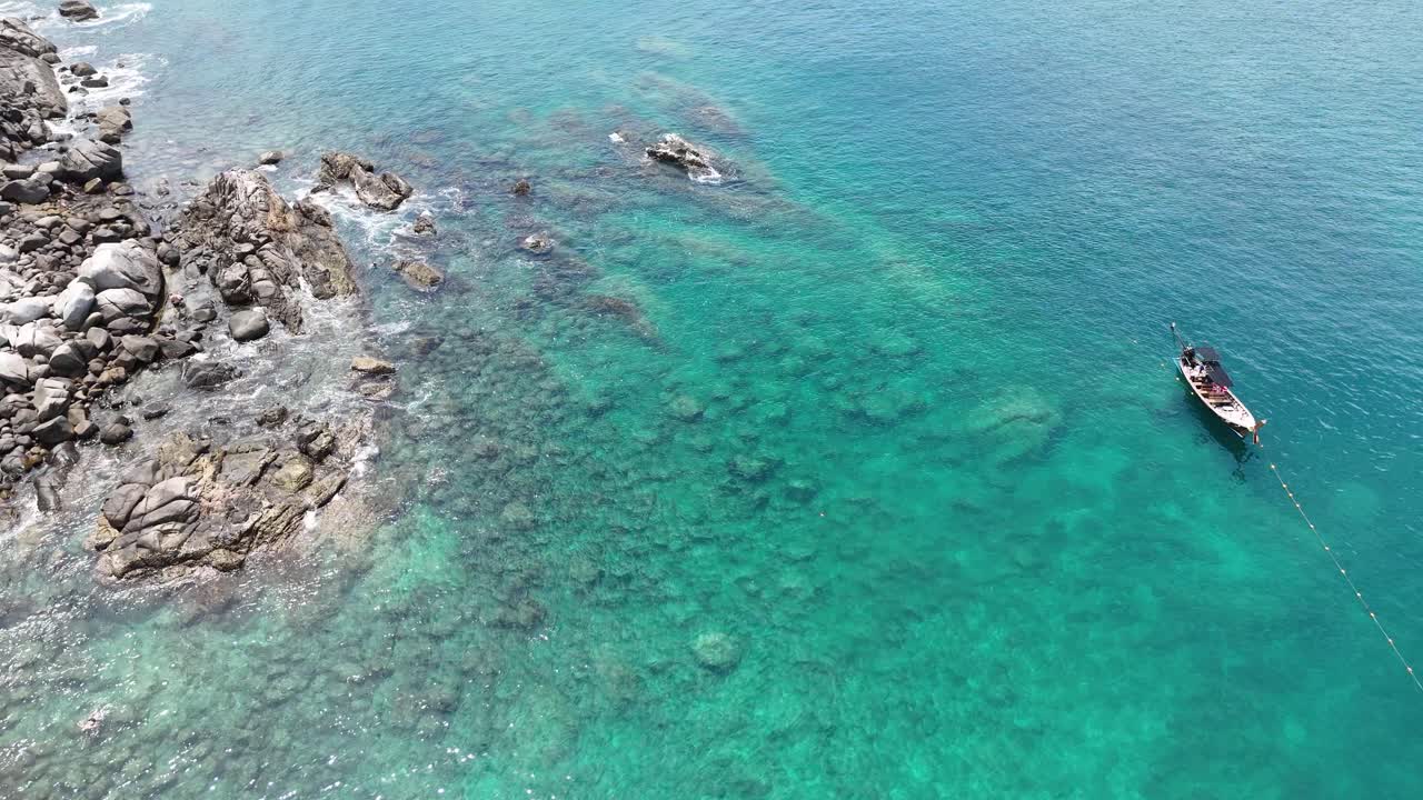 Hava çekimi, Tayland'ın Phuket şehrindeki kayalık kıyılar yakınında demirlemiş bir uzun kuyruklu tekneyi, berrak turkuaz suları ve mercan resiflerini gözler önüne seriyor.