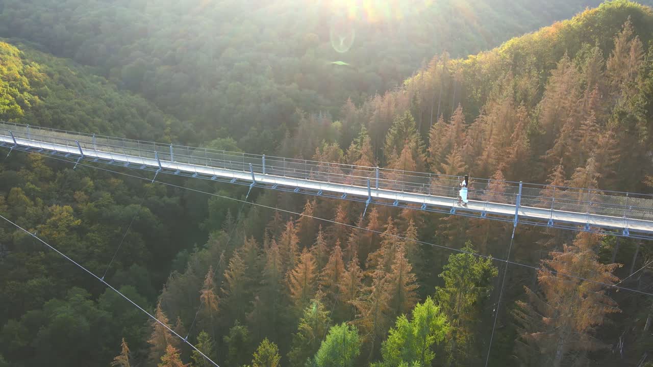Aerial shot of young woman walking across Geierlay suspension bridge in Western Germany