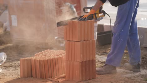 el trabajador está cortando a través de ladrillos creando ladrillos más pequeños para una pared aislante de albañil