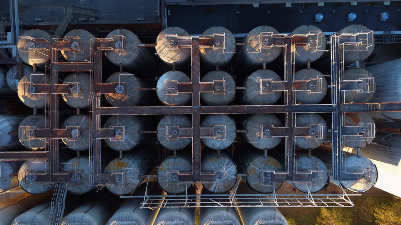 Aerial of a brewery cellar with stainless steel fermentation vessels, interconnected piping, manifolds and access gantries, illustrating process flow and industrial layout