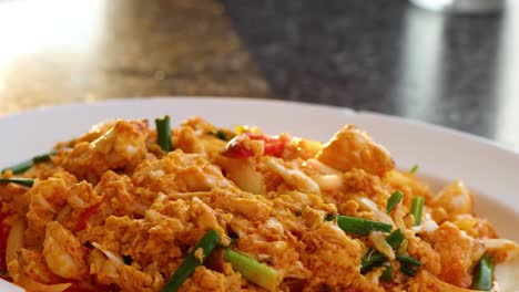 close-up of hands setting a colorful crab stir fry on a table, showcasing its rich texture and garnishes.