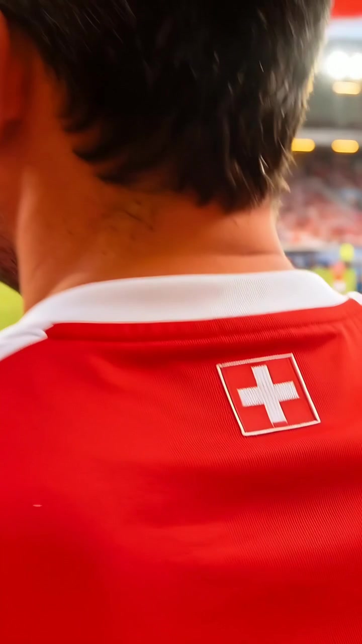 Vídeo vertical: Bandeira suíça tremulando, atraindo a câmera para um torcedor na arquibancada com camisa da cruz vermelha, apoiando