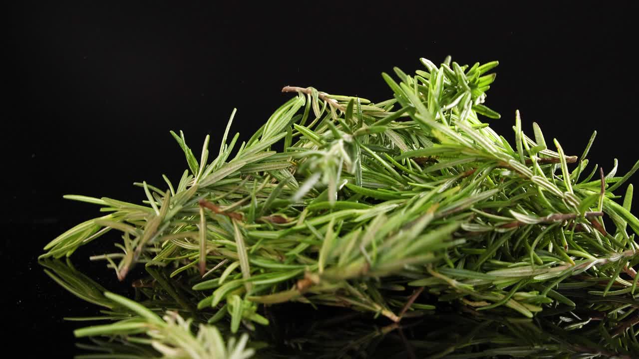 A bunch of rosemary drops onto a reflective black surface, captured in slow motion with dramatic lighting