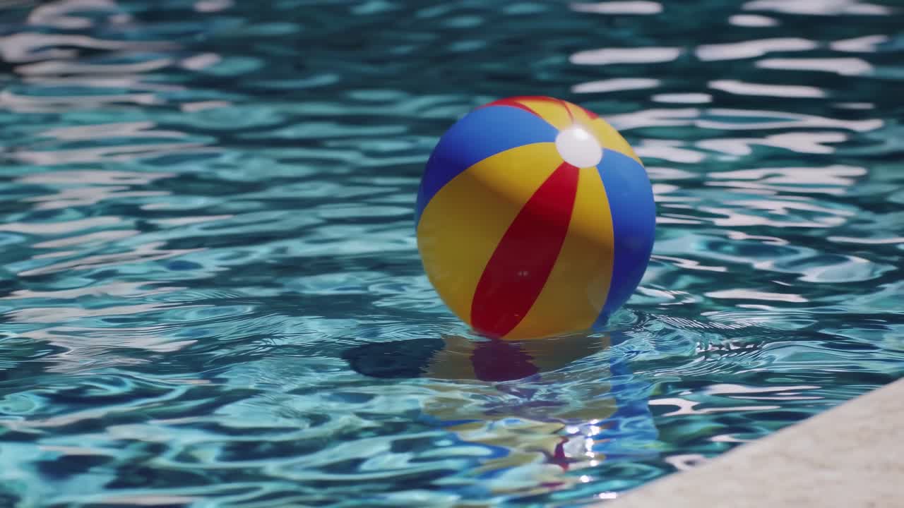 Vibrant beach ball gently floating on the tranquil, rippling surface of a swimming pool, creating a picturesque scene of summer relaxation and leisure