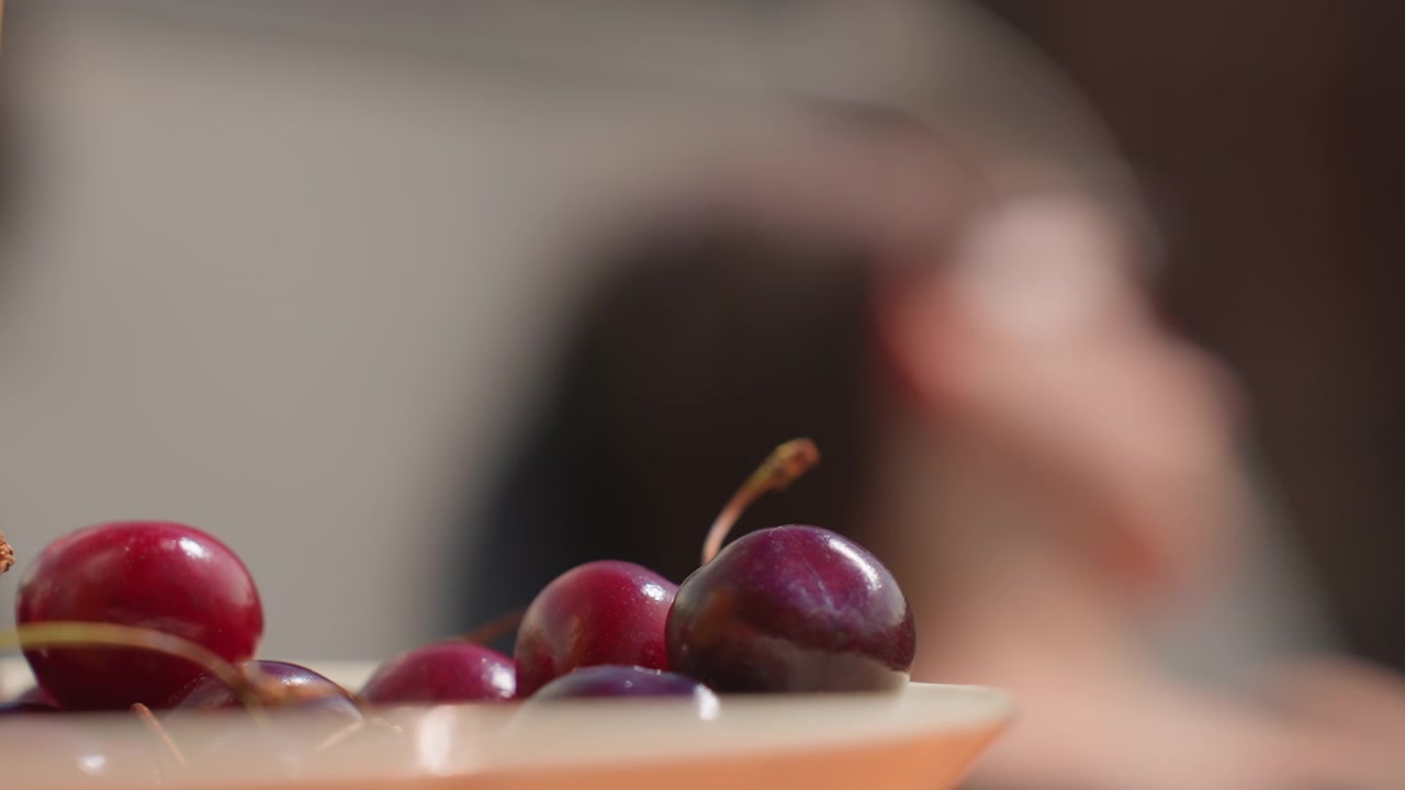 Ripe red cherries rest on light colored plate with soft focus background and subtle camera movement. scene emphasizes glossy texture of fresh fruit in natural lighting