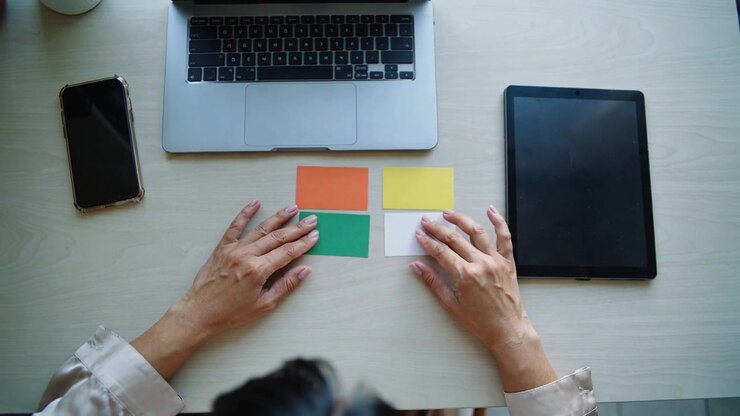Mani che entrano, donna in camicetta beige che sistema post-it sulla scrivania per la pianificazione, con un laptop.
