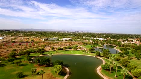 aerial slow push in from the edge of a pond at granada park toward the metro phoenix, ​skyline