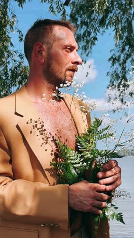 man in beige jacket with flowers by a lake