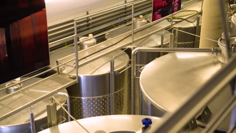 una toma panorámica de izquierda a derecha del almacenamiento de vino en barriles de acero en una bodega, que muestra el proceso de almacenamiento