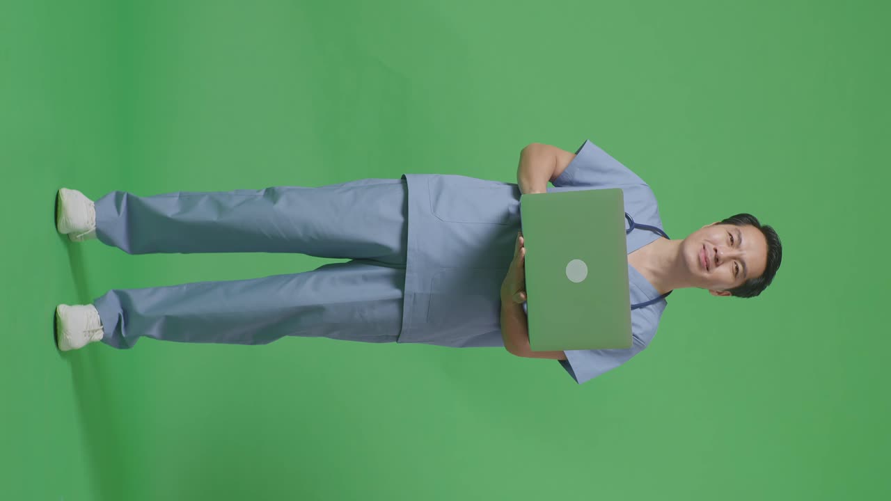 cuerpo lleno de médico masculino asiático con estetoscopio sosteniendo una computadora portátil y sonriendo en el fondo de la pantalla verde en el hospital