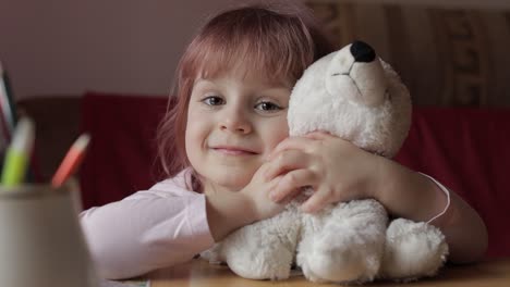 a young girl with pink hair smiling at the camera while holding a white teddy bear