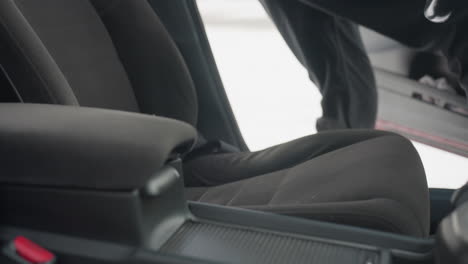 close up of interior showing car seat and center console with door open as person enters vehicle and sits down, resting hand on lap, snow visible outside suggesting cold winter day
