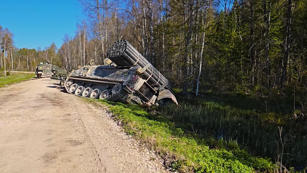 Rare footage of a Challenger 2 4034 combat engineering vehicle tank with an excavator arm and mine plough fallen into a ditch from a gravel dusty brown road in a marshland forest during a sunny day