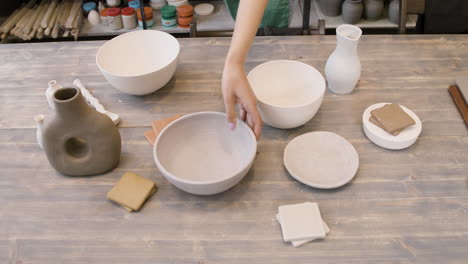 gros plan d'une femme méconnaissable mettant un bol en céramique et une cruche d'argile sur une table dans le magasin de poterie