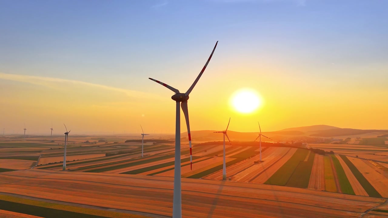 Sunset over wind turbine farm in countryside, Austria. Elevated drone shot of clean energy generators standing across agricultural fields.