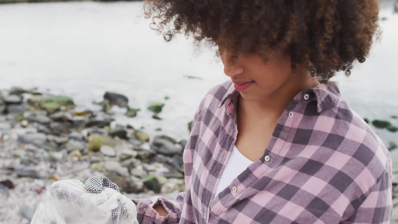 Ritratto di donna afroamericana con un sacchetto di plastica in piedi sulle rocce vicino al mare