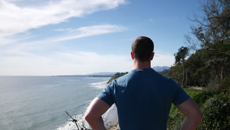 A-fit,-strong-man-standing-proud-after-a-successful-climb-on-the-edge-of-an-ocean-cliff-nature-hiking-trail-in-Santa-Barbara,-California-SLOW-MOTION