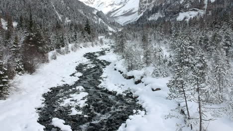 drone follows the course of a river in a snowy mountainous environment in the swiss alps