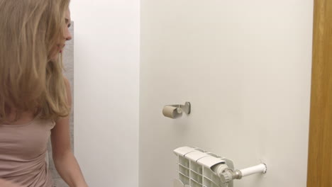 a woman is sitting on a toilet and running out of toilet paper