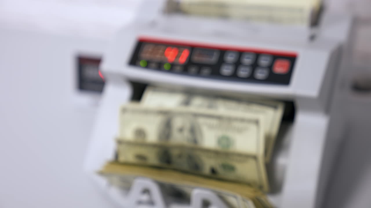Counting dollar bills. Money counting machine with 100 dollar banknotes. Female's hand holds a pack of US national paper currency. Finance concept. Close-up. Blurred background.
