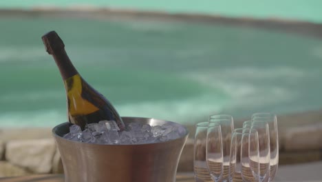 a waiter delivers a bottle of champagne on ice to a poolside table at a luxury resort