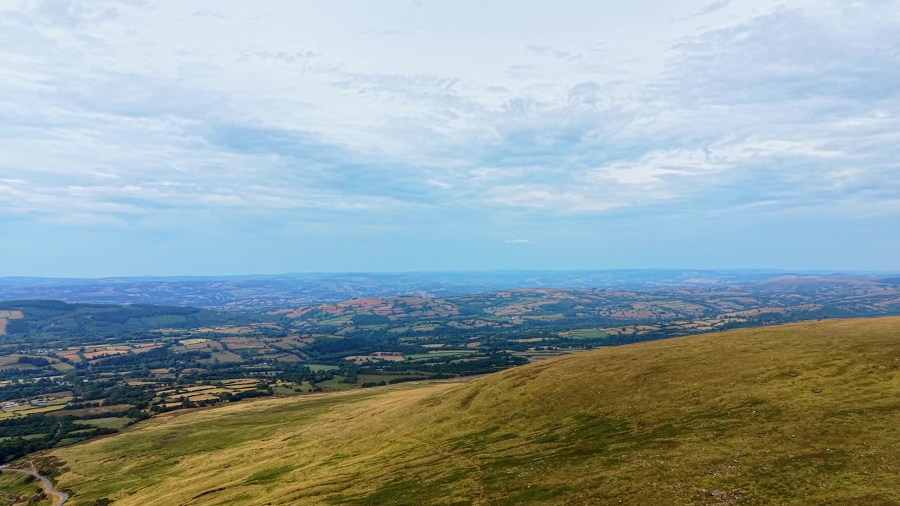 Vista in lenta ascesa sui Brecon Beacons con brughiera e campi estesi sullo sfondo