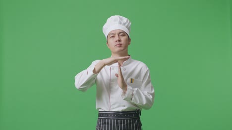 Asian Man Chef Looking At Camera And Showing Time Out Hands Gesture While Standing In The Green Screen Background Studio
