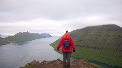 Unrecognizable-female-hiker-outstretches-her-arms-while-observing-Faroe-Islands-from-Klakkur-Mountain