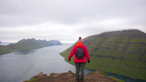una excursionista femenina irreconocible extiende sus brazos mientras observa las islas feroe desde la montaña klakkur