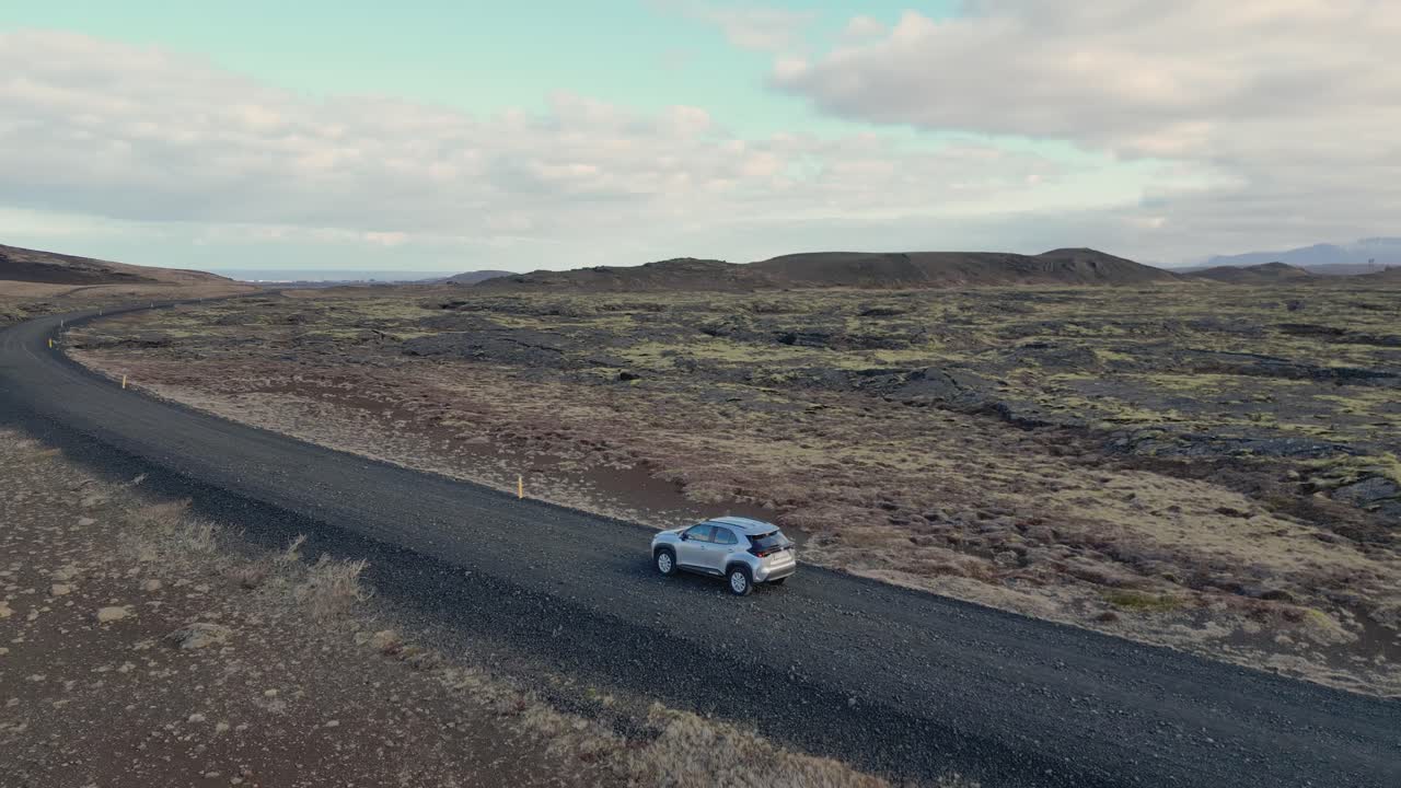 un coche conduce a través del paisaje estéril de islandia, rodeado de rocas volcánicas y musgo