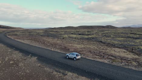 A-car-drives-through-Iceland's-barren-landscape,-surrounded-by-volcanic-rock-and-moss