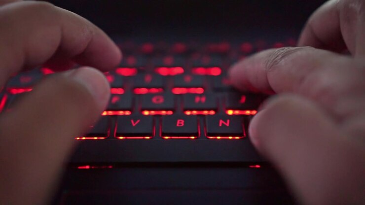 Hænder taster på et rødt baggrundsbelyst tastatur, digital livsstil, programmering og computerbrug.