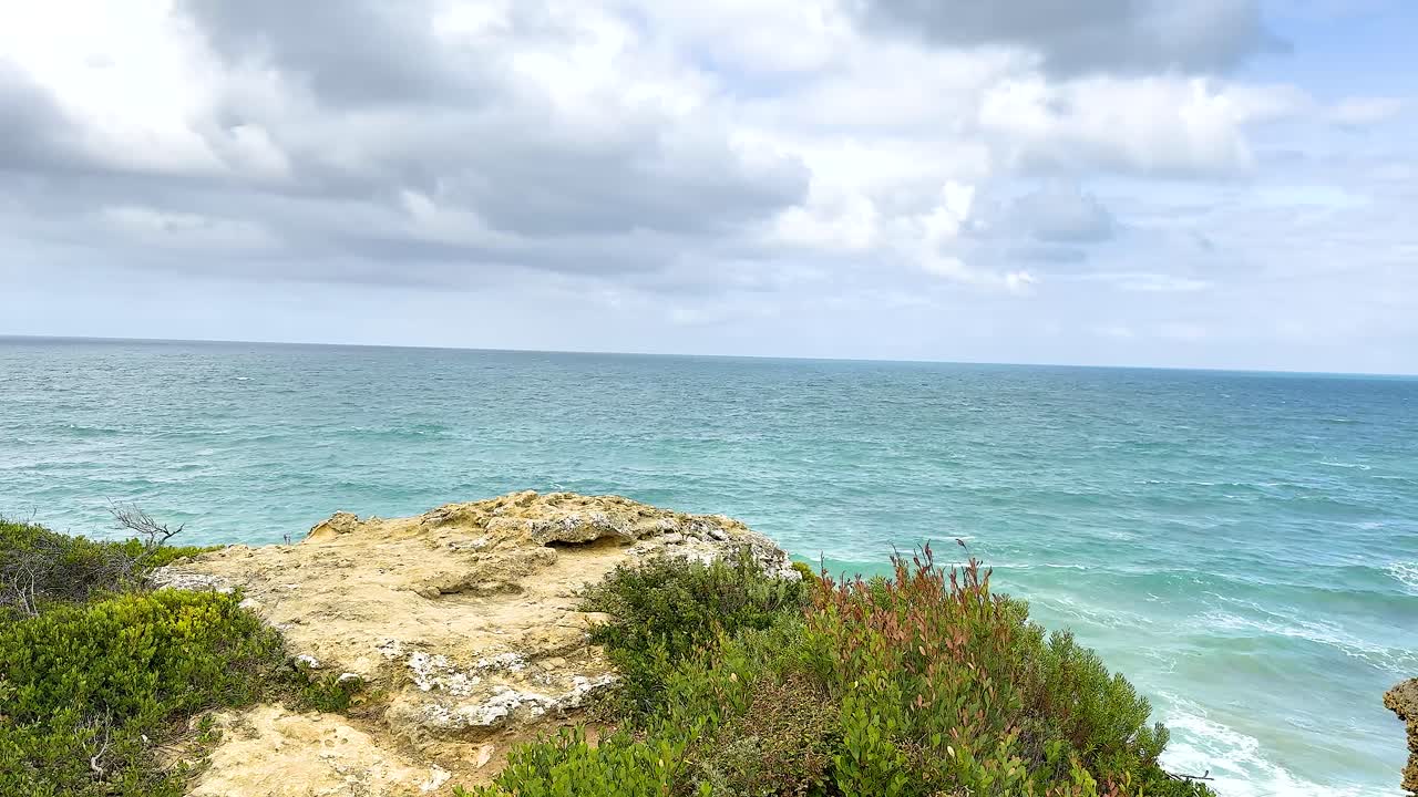 A tranquil ocean scene with cliffs and greenery under a partly cloudy sky, captured along the Great Ocean Road