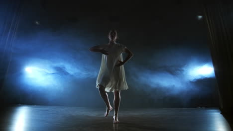 Modern-dance-woman-in-a-white-dress-dances-a-modern-ballet-jumps-on-the-stage-with-smoke-in-the-blue-spotlights.