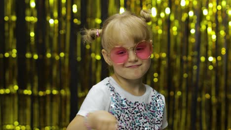 Child-smiling,-pointing-fingers-at-camera.-Girl-posing-on-background-with-foil-golden-curtain