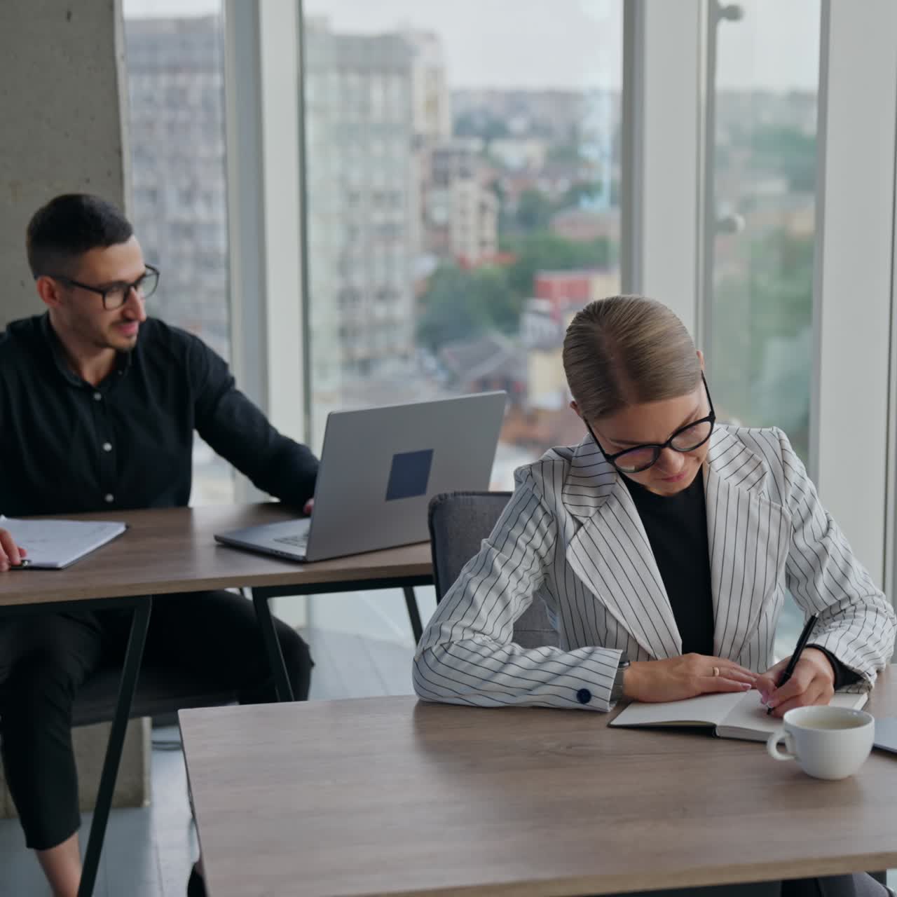 Persone impegnate nel loro lavoro in ufficio sedute alle scrivanie. Dipendenti che risolvono problemi di lavoro in un grande ufficio luminoso con finestre panoramiche e vista sfocata sul paesaggio urbano