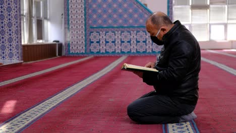 man wears mask and reads the quran in mosque