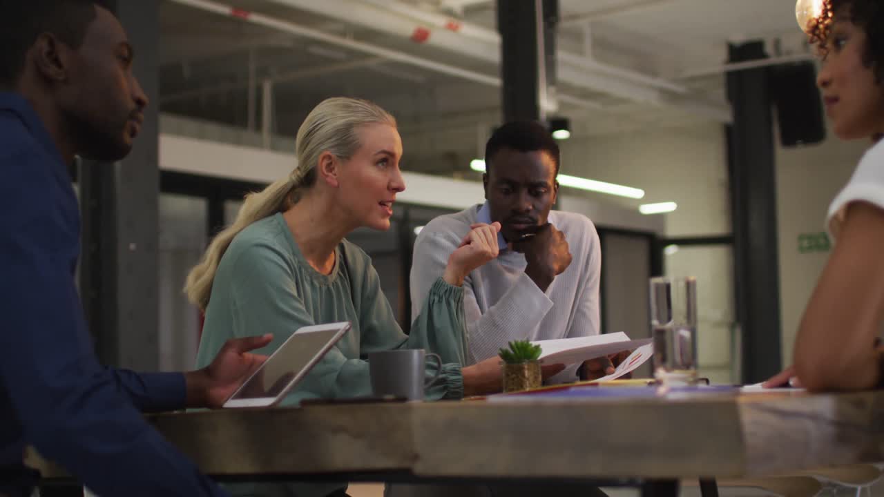 Diverse group of business colleagues talking in a meeting room using tablet pointing to document
