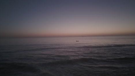 Stunning-view-of-boat-over-huge-ocean-with-orange-sky,-boats-illuminated,-Portugal