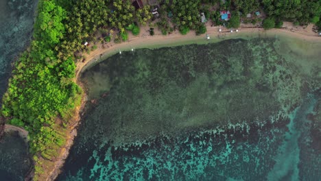 una vista aérea de arriba hacia abajo de una zona costera en las filipinas, con pequeñas chozas y barcos anidados cerca de aguas prístinas y claras