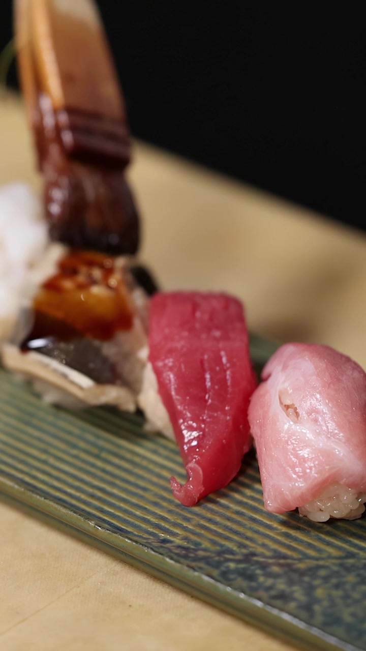 Primo piano di uno chef che applica salsa di soia su sushi nigiri di alta qualità usando un pennello.